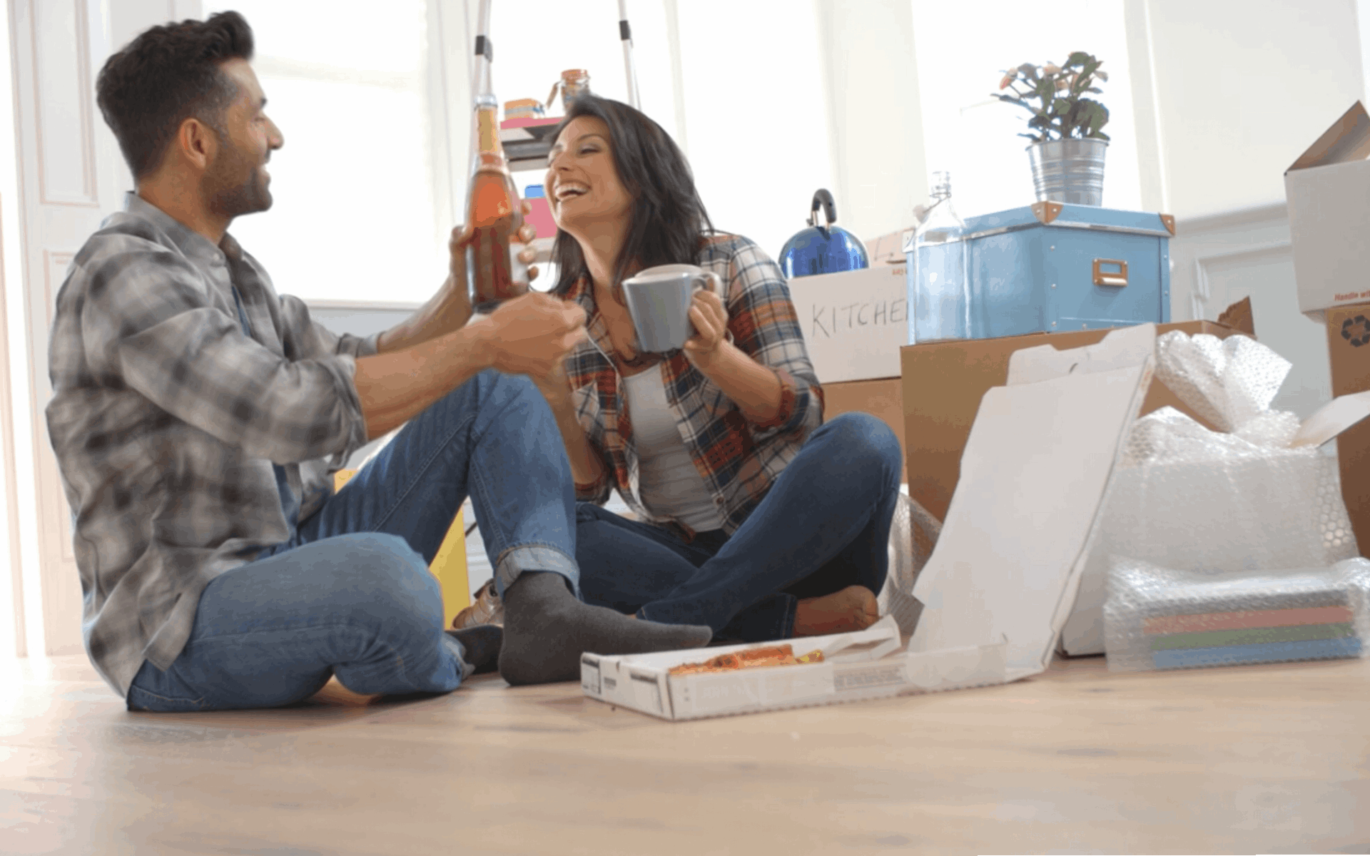 Couple celebrating on the floor of their new home with champagne and pizza